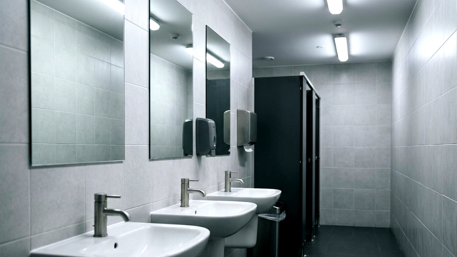 An empty commercial washroom with three wall-mounted basins and mirrors, clean and unoccupied.